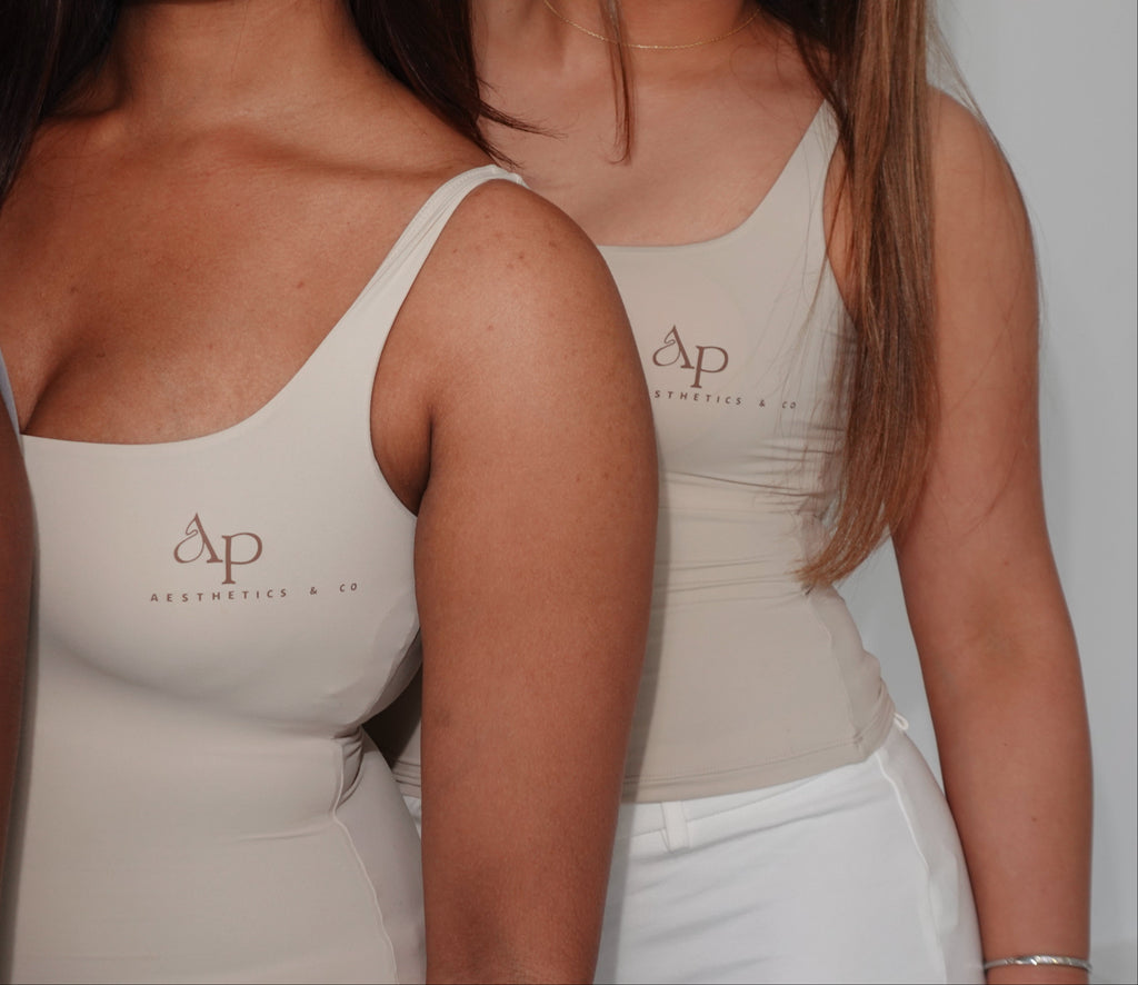 Two women wearing beige tank tops with a logo, standing close together.